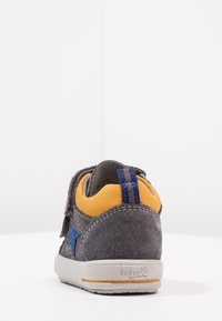 Sneaker grigio in suede per bambini con colletto in tessuto giallo, dettaglio a stella blu e suola bianca con il nome del marchio "superfit" visibile sul tallone.