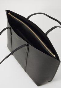 Zwarte leren tote bag met een gladde textuur, uitgerust met een gouden rits, twee lange handvatten en een open bovenkant. Interieur is van zwart stof.