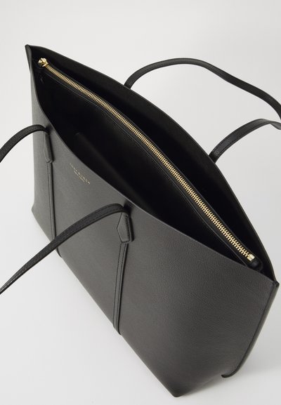 Sac fourre-tout en cuir noir avec une texture lisse, doté d'une fermeture éclair dorée, de deux longues poignées et d'un dessus ouvert. L'intérieur est en tissu noir.