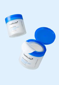 Behållare av Medicube Zero Pore Pad, vit burk med blå lock, visar en texturerad pad som delvis dragits ut, märkt med ingrediensinformation.