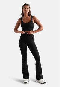 Schwarzes, geripptes Crop-Top und hochgeschnittene, ausgestellte Leggings, beide aus Stretchstoff. Glatte Textur mit dezentem Logo-Detail am Bund.