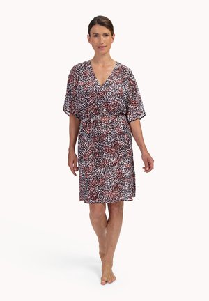 Vrouw die blootsvoets loopt en een knielange jurk met V-hals draagt, bedrukt met een abstract dierenpatroon in rood, zwart en wit, met korte mouwen.