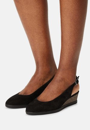 Black suede slingback wedge shoes with rhinestone-studded heel worn on brown-skinned feet against a plain background.