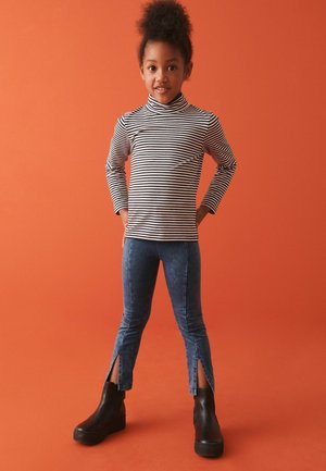 Schwarz-weiß gestreiftes Langarmoberteil mit Stehkragen, kombiniert mit blauen Denim-Look Leggings mit Seitenschlitzen und schwarzen Ankle Boots.