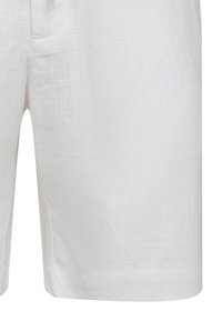 I pantaloni corti bianchi in lino presentano una superficie texturizzata, lunghezza fino a metà coscia e un design casual con tasche laterali. Nessuna ferramenta o chiusura visibile.