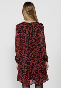 Rochie florală roșie și neagră cu mâneci lungi, din țesătură transparentă, cu talie strânsă și manșete cu buton, având un model abstract vibrant.