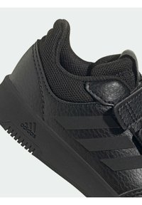 Černá sportovní obuv s texturovaným koženým svrškem, síťovanými detaily a třemi horizontálními pruhy. Má pevnou gumovou podrážku a nastavitelný pásek.