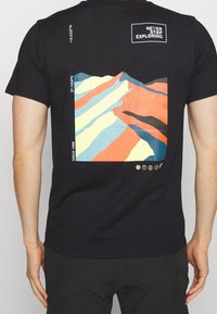 Camiseta negra de algodón con un gráfico abstracto colorido de montañas en la parte trasera, que presenta rayas de naranja, amarillo y azul. La parte delantera tiene un parche con logo.