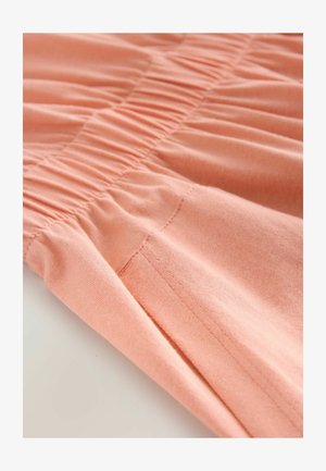 Tissu de couleur pêche avec une texture froncée, présentant des détails de couture subtils et une finition douce. Le matériau semble lisse et léger.