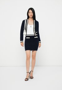 Completo due pezzi navy composto da una giacca cropped in maglia testurizzata con rifiniture bianche e bottoni dorati, abbinata a una gonna aderente. Tacchi neri.