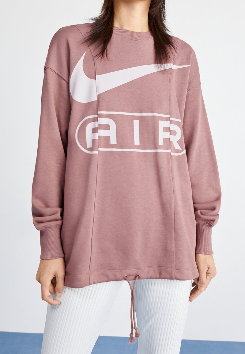 Volný růžový svetr s velkým bílým logem Nike a grafikou "AIR". Obsahuje žebrované manžety a stahovací lem pro nastavitelnost.