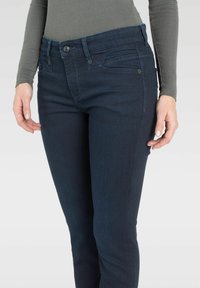 Granatowe dżinsy o slim fit, posiadające klasyczny pięciokieszeniowy krój, zamek na guzik z przodu oraz subtelne detale przeszyć.