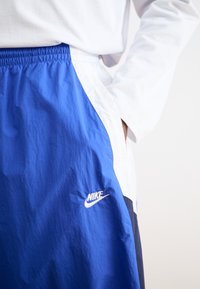 Nike šorti zilos un baltos toņos, ar teksturētu audumu, elastīgu jostasvietu un Nike logo baltā krāsā kreisajā pusē.