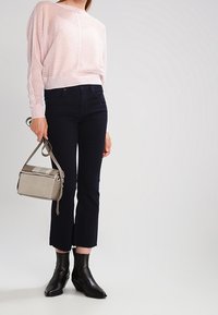 Un pull en tricot texturé rose pâle associé à un jean en denim foncé, des bottines noires à la cheville et un petit sac bandoulière beige.