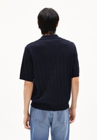 Navy gebreid poloshirt met ribbelpatroon, korte mouwen en een klassieke kraag. Draag het met lichtblauwe jeans met stiksels op de achterzak.