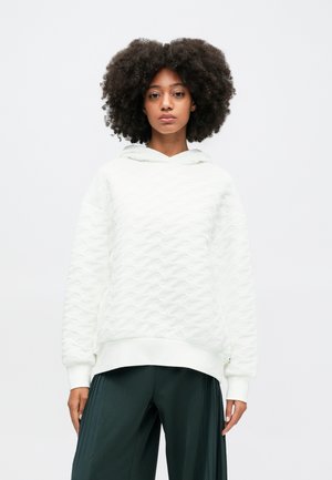 Sudadera blanca texturizada con un patrón de olas, que presenta una capucha y puños acanalados, combinada con pantalones de pierna ancha verde oscuro.