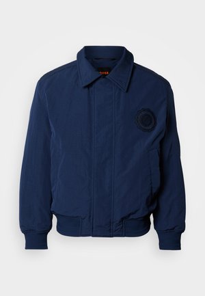 Tmavomodrá bomber bunda s golierom, rebrovanými manžetami a lemom, vyšívaným logom na hrudi a hladkou, textúrovanou tkaninou.