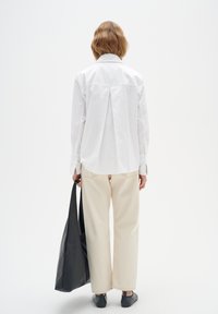 Camisa blanca de manga larga con pliegues en la espalda, pantalones de cremoso de pierna ancha y bolso de cuero negro. Diseño casual y minimalista con texturas suaves.