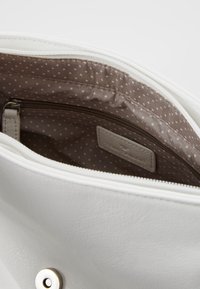 Weiße Lederhandtasche mit braunem gepunktetem Innenfutter, Reißverschlusstasche und Markenlabel. Glatte Textur mit sicherem Reißverschluss.
