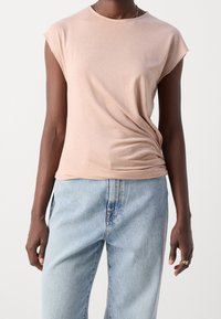 Camisa de color melocotón, de manga corta, con un escote redondo y un corte relajado. Combinada con unos jeans de mezclilla sueltos de color azul claro.
