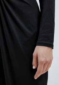 Schwarzer Stoff mit glatter Textur, der locker fällt. Eine Hand mit hell lackierten Nägeln befindet sich in der Nähe des Stoffedges.