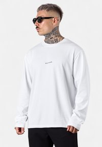 Weißes Langarm-T-Shirt aus Baumwolle mit einem kleinen gedruckten Logo "esteem" auf der Brust. Das Modell trägt schwarze Sonnenbrillen.