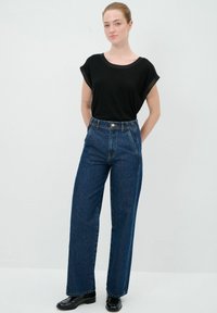 Černý krátký rukáv top kombinovaný s vysokým pasem širokými modrými džínami s předním zapínáním na knoflík a postranním švem.