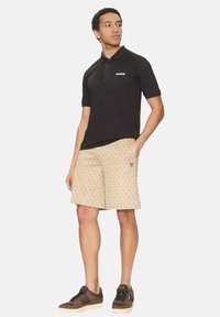 Polo negro de manga corta con cremallera frontal y logo blanco. Pantalones cortos beige con un patrón repetitivo y detalle del logo rojo. Zapatillas marrones.