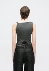 Κοντό γκρι τοπ χωρίς μανίκια με σφικτή υφή και λεπτομέρεια με δεμένη τιράντα. Συνδυασμένο με σκούρο τζιν.