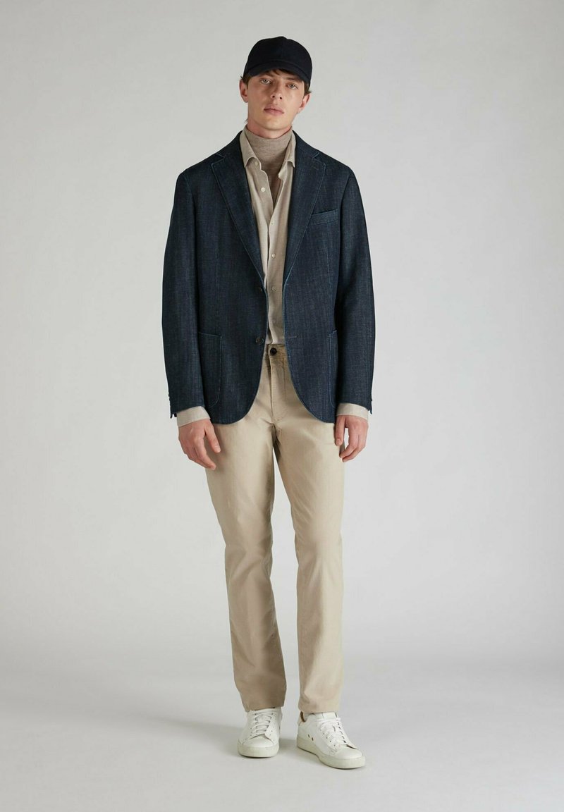 Granatowy marynarka z wyciętymi klapami, beżowa koszula i kremowe chinosy. Białe trampki dopełniają stylizację, nadając jej nowoczesny, swobodny wygląd.