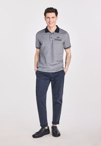 Szary podkoszulek z granatowym kołnierzykiem i paskowymi akcentami, w połączeniu z granatowymi spodniami i czarnymi sneakersami. Gładka tkanina i dopasowany krój.