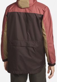 Bunda s bloky barev v barvách bordó, hnědé a olivově zelené. Hladká, lehká látka s kapucí a elastickými manžetami. Detail zadní kapsy.