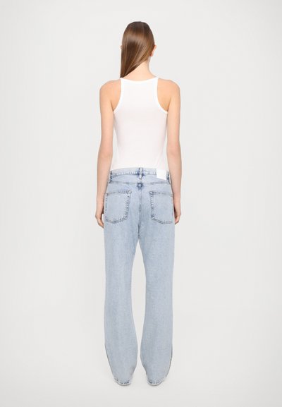 Light blue denim jeans with a loose fit, featuring two back pockets and a white label at the waistband. Paired with a white tank top.