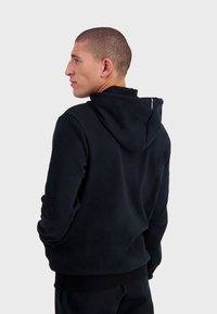 Sudadera de forro polar azul marino con capucha ajustable, puños y bajo acanalados. Presenta una pequeña etiqueta en la parte posterior del cuello. Textura suave y corte relajado.