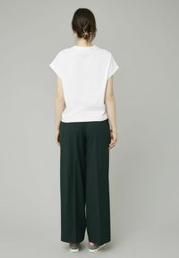 Haut blanc à manches courtes, coupe ample, associé à un pantalon large vert foncé et des chaussures de sport avec des accents roses. Design minimaliste.