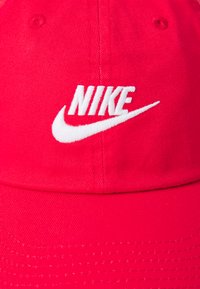 Piros szövetsapka ívelt karimával, elöl fehér hímzett Nike logóval és finom textúrált varrási részletekkel.