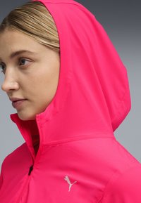 Ροζ εφαρμοστή ζακέτα με ψηλό γιακά, κλείσιμο με φερμουάρ και λογότυπο ως διακοσμητικό. Λείο, ελαφρύ ύφασμα με υφασμένη κουκούλα.