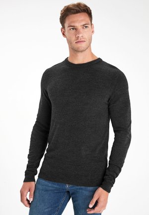 Mörkgrå, stickad tröja med långa ärmar och rund hals, som bärs över blå jeans. Slät textur, klassisk design, inga mönster.