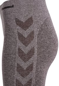 Zbliżenie szarych, teksturowanych legginsów z czarnymi wzorami w jodełkę i logo "hummel" blisko pasa.