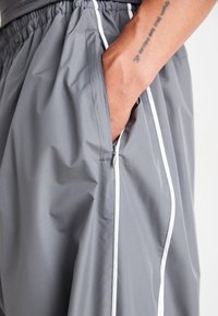 Gray athletic shorts with a lightweight, smooth texture. Features a white side stripe and a side pocket with a zipper closure.