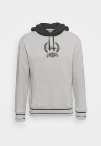 Sudadera gris claro con doble capucha negra, bolsillo central en la parte delantera y puños elásticos. Presenta un logo negro bordado y rayas decorativas.