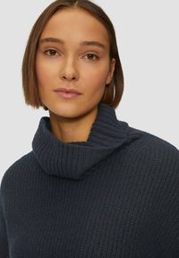 Donkerblauwe gebreide trui met een geribde col. De stof heeft een gestructureerd patroon, wat warmte en comfort biedt.
