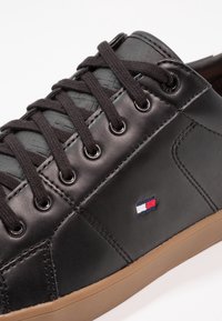 Černé kožené tenisky s texturovanou tkaninou na jazyku, černými tkaničkami, kovovými očky a malým vícerozměrným logem na boku.