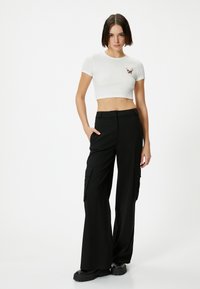 Top corto blanco con textura acanalada y detalle bordado, combinado con pantalones cargo negros de pierna ancha que cuentan con bolsillos laterales y un acabado suave y mate.