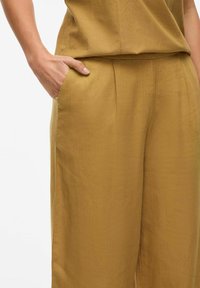 Pantalones de pierna ancha en un cálido tono mostaza, fabricados en un tejido ligero, que presentan bolsillos laterales y un ajuste relajado con una textura sutil.