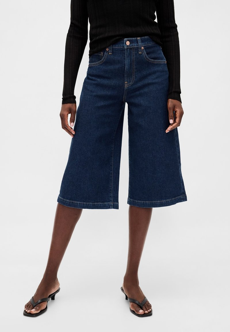 Denimculottes i mörkblått med vid benform, framfickor, knappstängning och subtila sömnadsdetaljer vid fållen.