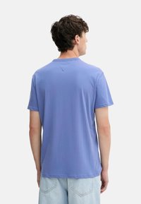 Camiseta de algodón azul claro con cuello redondo y mangas cortas. La parte trasera presenta un detalle de costura triangular, una textura suave y un corte relajado.