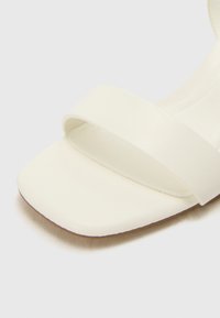 White block-heeled sandal with two wide matte straps. Square toe and flat sole, featuring a smooth texture and minimalistic design.