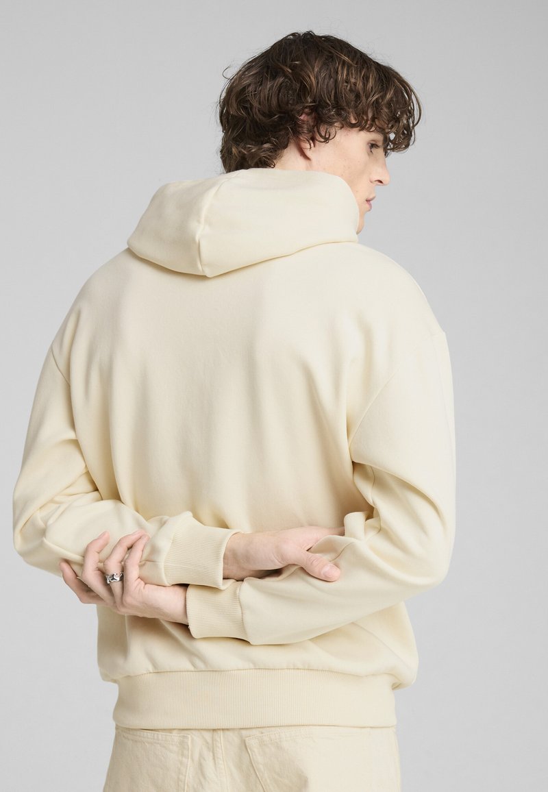 Šviesiai kreminės spalvos kreminė su gobtuvu, pasižyminti laisvu siluetu, raukiniais ant rankovių ir dideliu gobtuvu. Lygi tekstūra su minimaliais siuvimo detaliais.