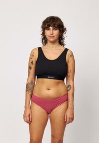 Zwarte katoenen sportbeha met een brede scoop halslijn en logoband; gecombineerd met roze bikini-onderbroek op taillehoogte. Gladde textuur, minimale uitstraling.